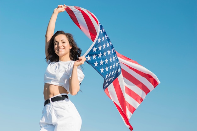 Free Photo mid shot young woman holding big usa flag and smiling