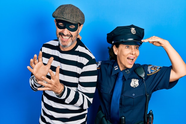 Free Photo middle age couple of hispanic woman and man wearing thief and police uniform very happy and smiling looking far away with hand over head. searching concept.