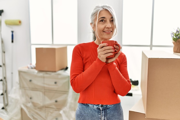 Free photo middle age greyhaired woman smiling confident drinking coffee at new home