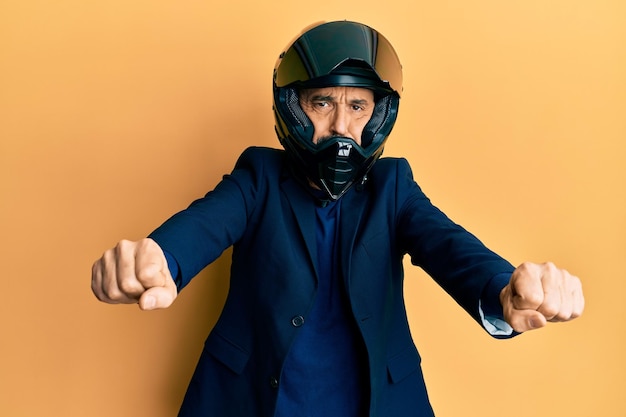 Free photo middle age hispanic man wearing motorcycle helmet doing moto symbol with hands puffing cheeks with funny face. mouth inflated with air, catching air.