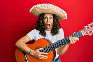 Free photo middle age hispanic woman holding mexican hat playing classical guitar celebrating crazy and amazed for success with open eyes screaming excited