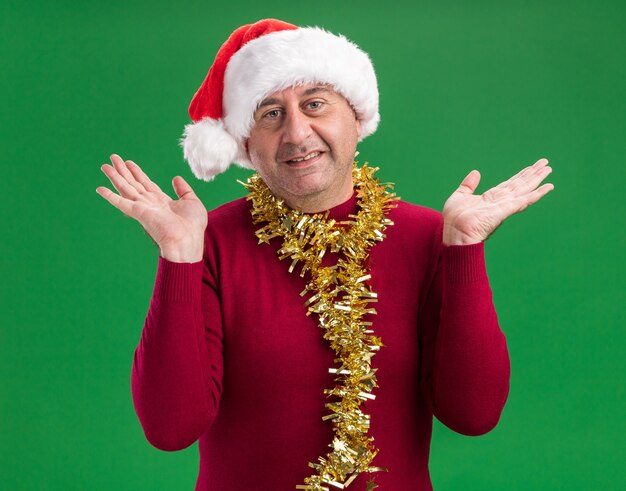 Middle age man wearing christmas santa hat with tinsel around neck  smiling with happy face with arms raised 