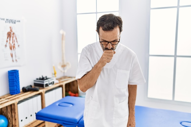 Middle age man with beard working at pain recovery clinic feeling unwell and coughing as symptom for cold or bronchitis health care concept