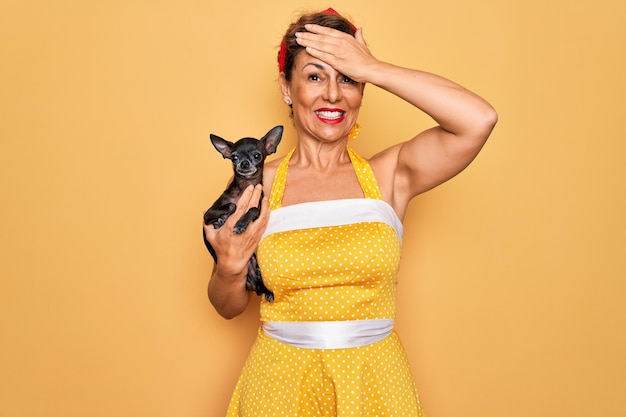 Free photo middle age senior pin up woman wearing 50s style retro dress holding chihuahua dog stressed with hand on head shocked with shame and surprise face angry and frustrated fear and upset for mistake