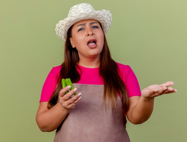 Free photo middle aged gardener woman in apron and hat holding halves of green chili pepper