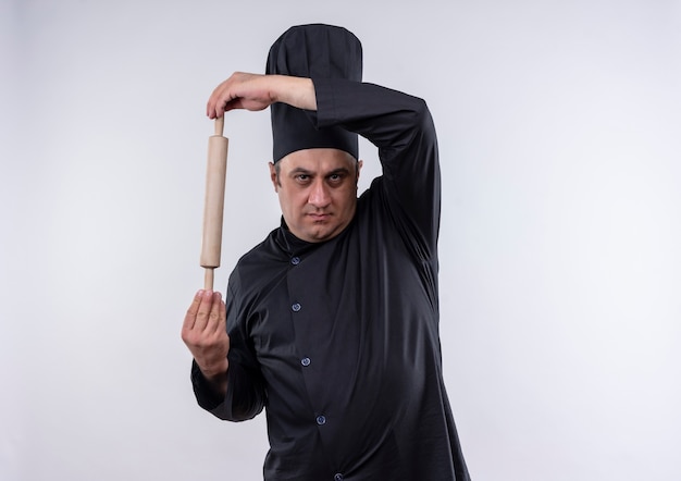 Free photo middle-aged male cook in chef uniform holding rolling pin on isolated white wall with copy space