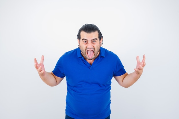 Middle aged man keeping hands in aggressive manner while sticking tongue out