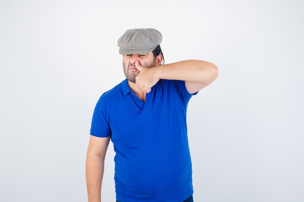 Free photo middle aged man pressing thumb on nose in polo t-shirt, ivy hat and looking cheerless