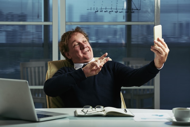 Free photo middle aged man taking selfies at his office desk