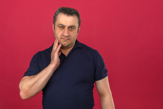 Middle aged man wearing polo shirt touching chin while thinking with serious face over isolated pink wall