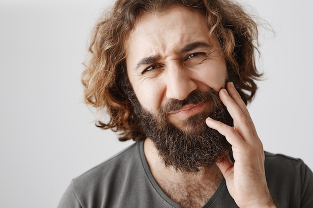 Middle-eastern bearded guy touching cheek and grimacing from pain, having toothache