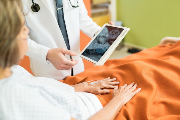 Free Photo midsection of doctor showing xray report on digital tablet to senior patient at hospital