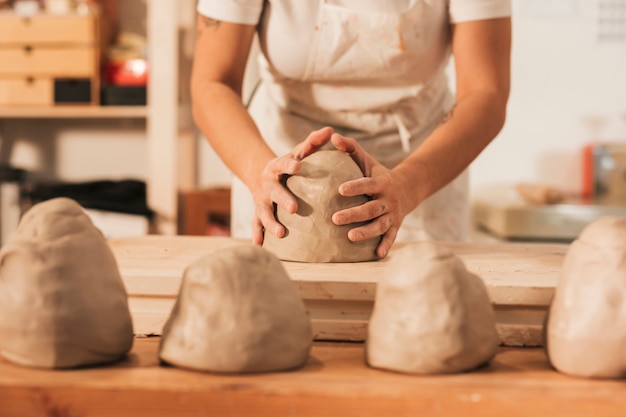 Midsection of female craftswoman giving shape to clay on wooden table