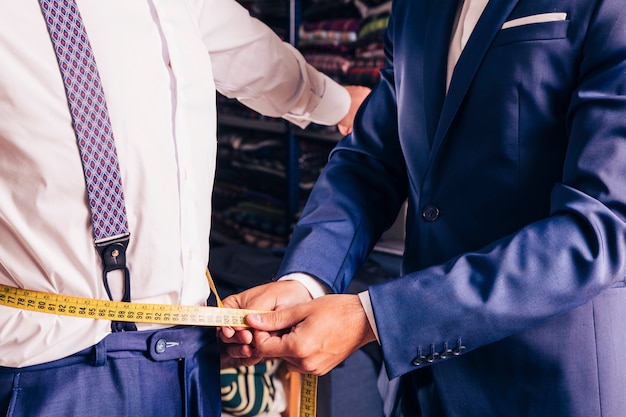 Free Photo midsection of a male tailor taking measurement of man's waist