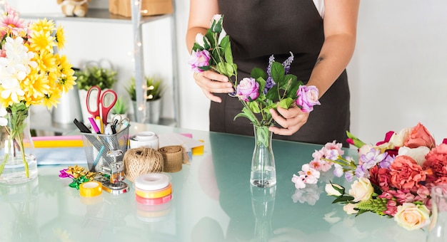 Midsection view of a female hand sorting flowers in vase on desk