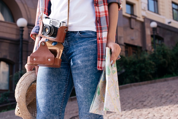 Free Photo midsection of woman holding map and hat with carrying camera while travelling alone