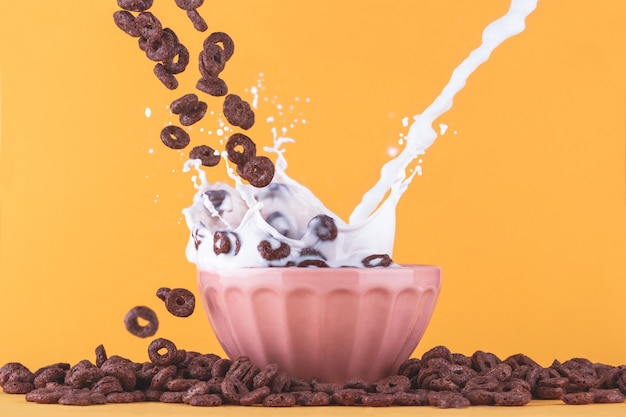 Milk cup with chocolate cereals falling around and milk splashing.