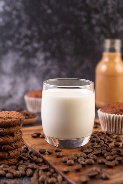 Free photo milk in a glass, complete with coffee beans, cupcakes, bananas and cookies on a wooden plate.