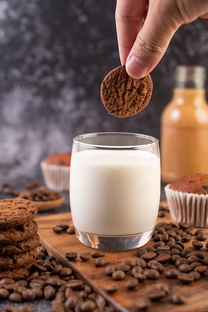 Milk in a glass, complete with coffee beans, cupcakes, bananas and cookies on a wooden plate.