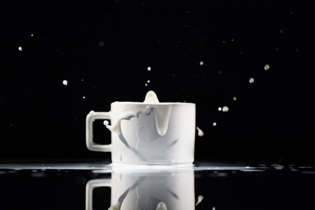 Free photo milk splashes in white cup on black background