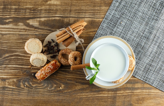 Milk with mint, biscuits, cloves, cinnamon sticks in a cup on wooden surface