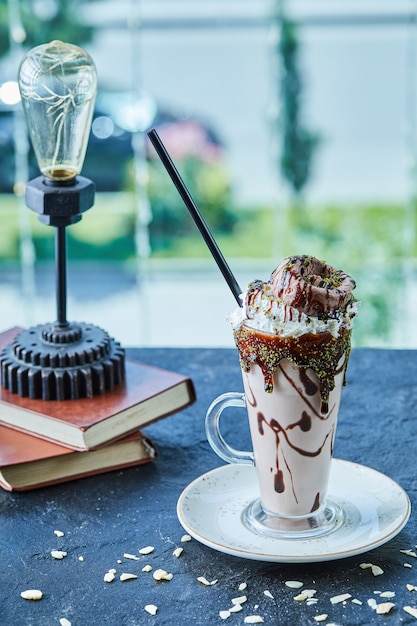 Free photo milkshake with cone, chocolate , sprinkles and books, lamp in the dark surface