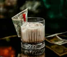 Free photo milky drink with ice cubes in whisky glass pinned with dollar