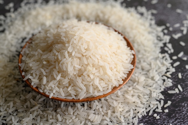 Milled rice in a bowl and a wooden spoon on the black cement floor.