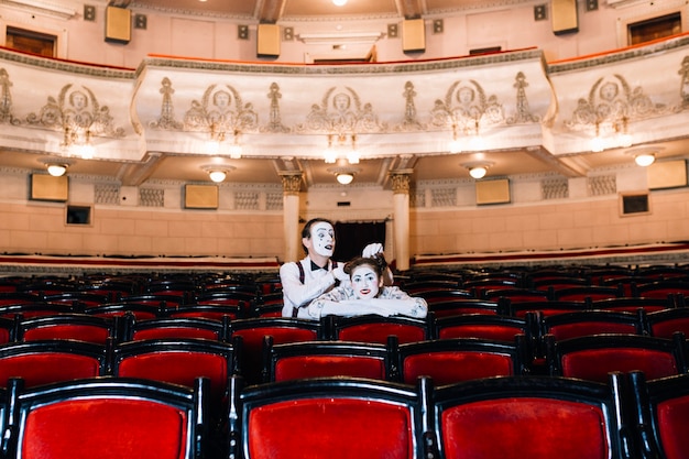 Free Photo mime male artist playing with female mime's hair sitting together on chair in auditorium