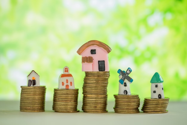 Mini house on stack of coins with green blur. 