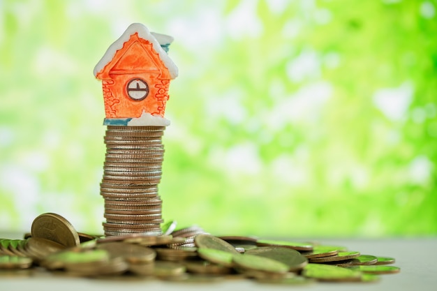 Mini house on stack of coins with green blur. 