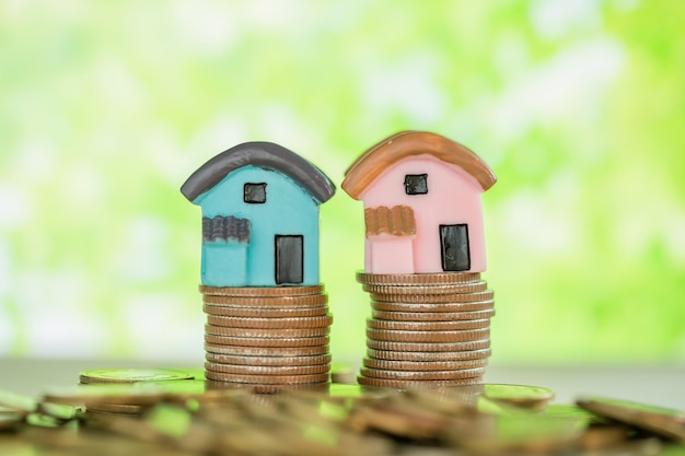 Mini house on stack of coins with green blur. 