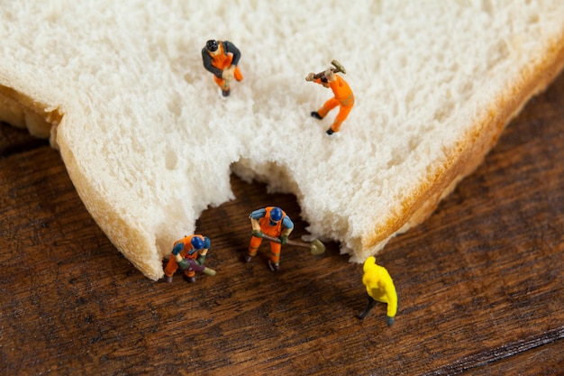 Free Photo miniature workers working on sliced of bread