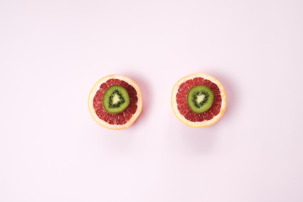 Free photo minimal fruit background top view of sliced citrus fruits grapefruit and kiwi on pink table top view flat lay