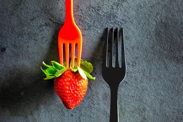 Minimalistic elegant, black fork and a strawberry on black table