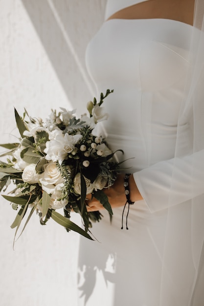 Minimalistic wedding dress for the bride and beautiful wedding bouquet made of white flowers and greenery, classy attire