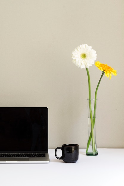 Free Photo minimalistic workplace with laptop and flowers in glass vase on desk 