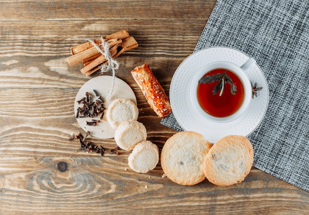 Minty tea with cinnamon sticks, biscuits, cloves in a cup on wooden surface