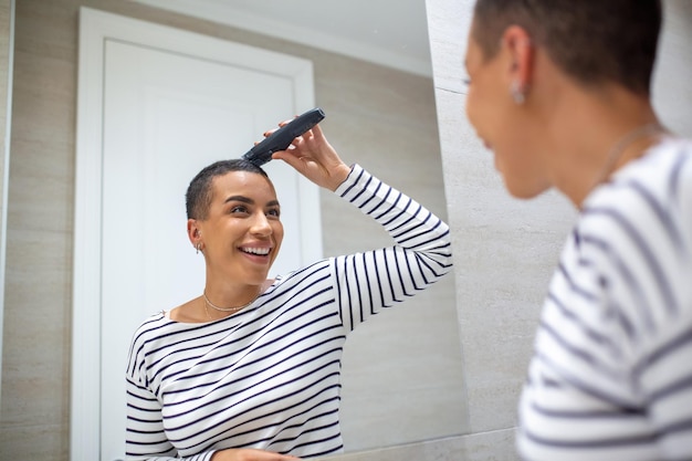 Mirror reflection of short haired woman in tank top using haircutting machine