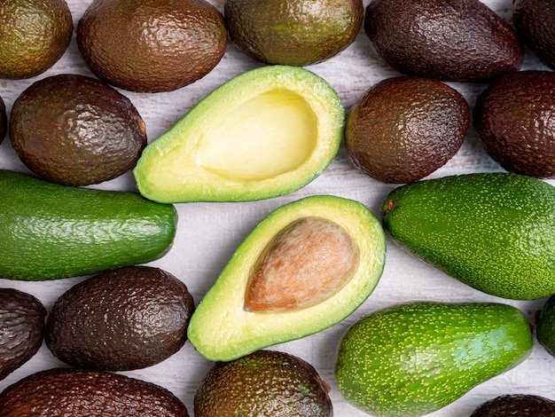 Mix of ripped and green avocados on white wooden board.