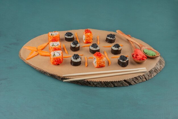 Mix sushi and spoons of pickled ginger and wasabi on wooden board.