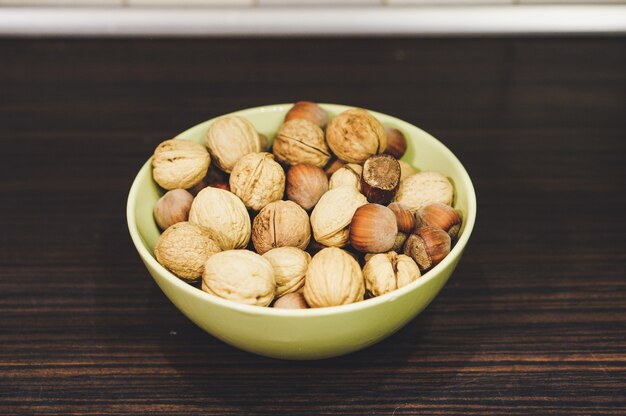 Mix of walnuts and hazelnuts in a yellow bowl on a wooden table