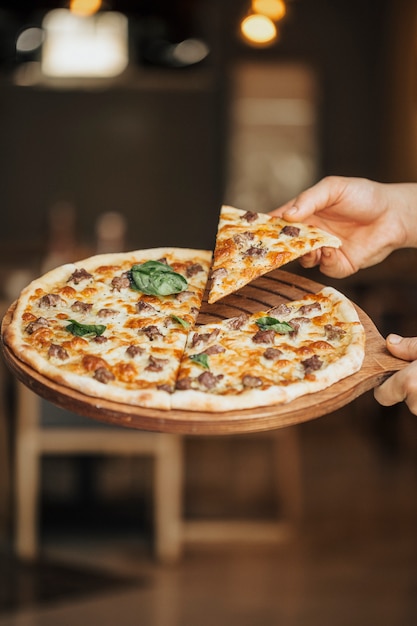 Free photo mixed ingredient pizza on a wooden board, taking a slice