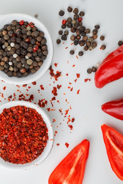 Free Photo mixed peppercorns in a plate with chili powder and red peppers close-up on a white wall