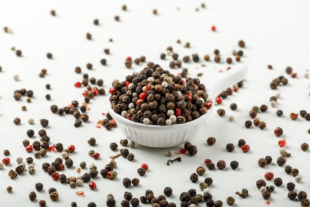 Free photo mixed peppercorns in a white scoop side view on spicy and white background