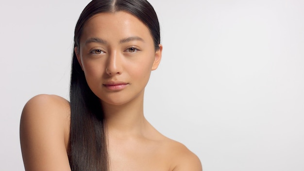 Free photo mixed race asian model in studio beauty shoot model poses to a camera straight hair combed to right side ideal skni and no makeup makeup head and shoulders crop watching to the camera