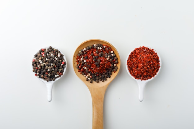 Mixed spice in a wooden spoon with peppercorns and cayenne pepper in scoops top view on a white background