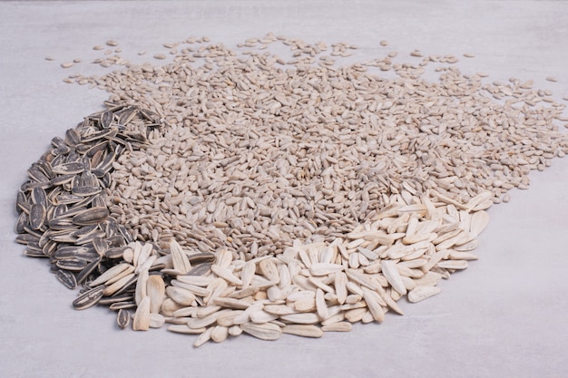 Mixed sunflower seeds scattered on white surface.