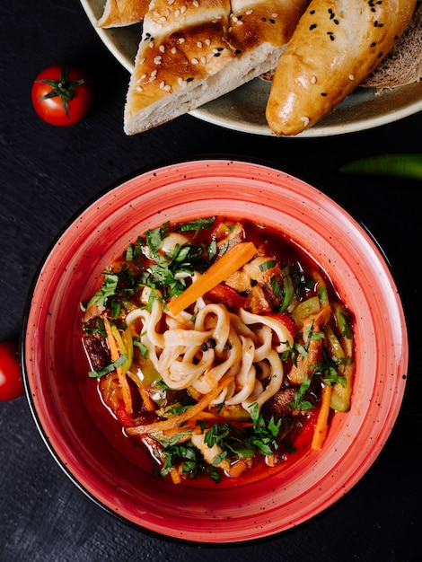 Mixed vegetable salad in red bowl with bread.