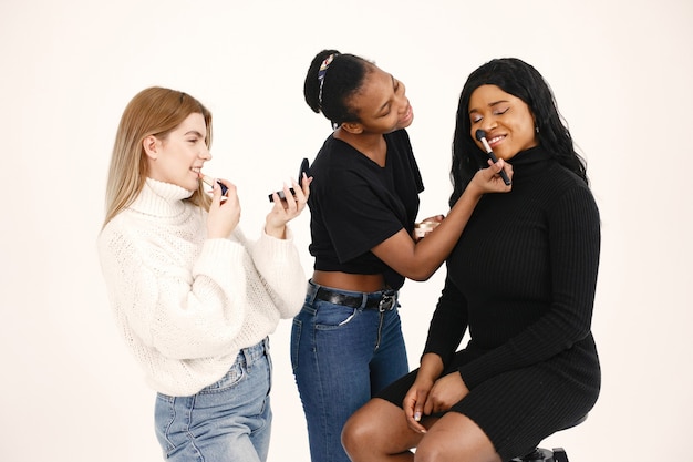 Free photo mixed women doing makeup to his girlfriend. multiracial friends posing isolated over white wall background.